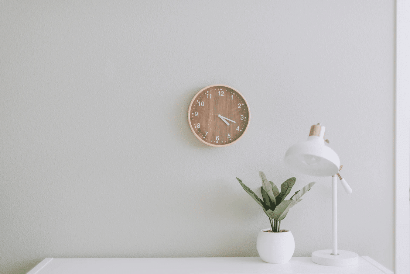 plain wall with clock and plant on desk
