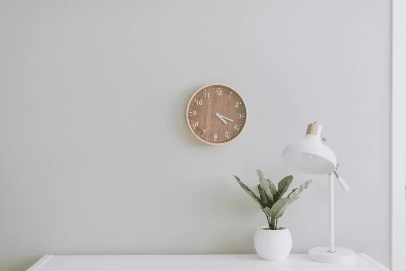 plain wall with clock and plant on desk